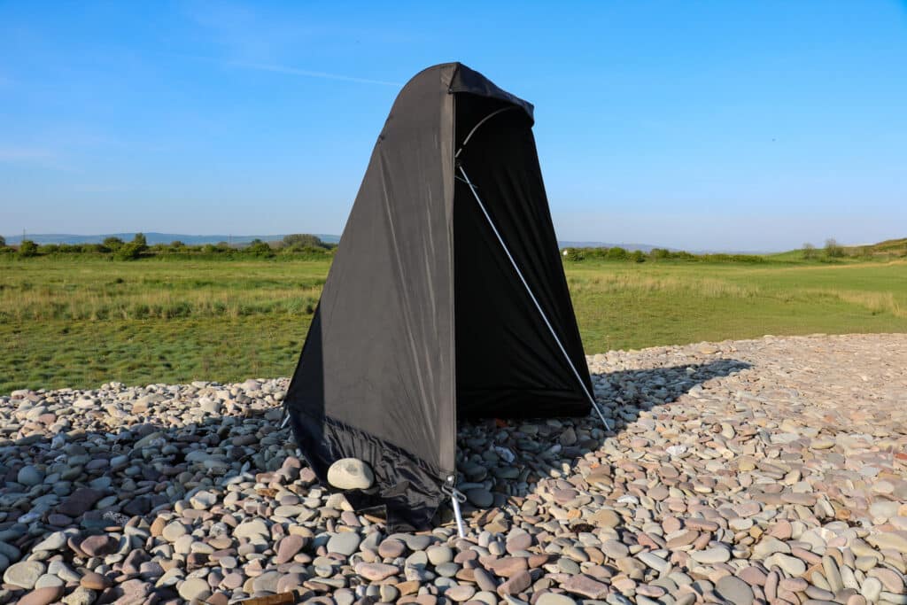 fishing tent on pebble beach in front of green grass field
