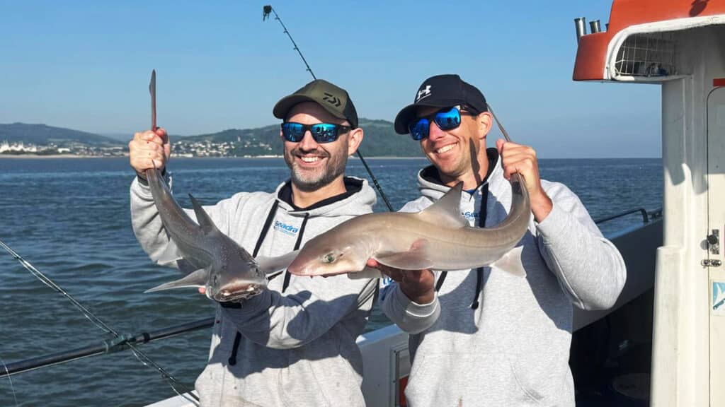 two men holding sharks for a picture on a boat