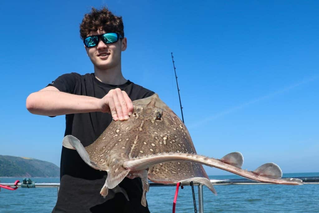 man holding a thornback ray on a boat